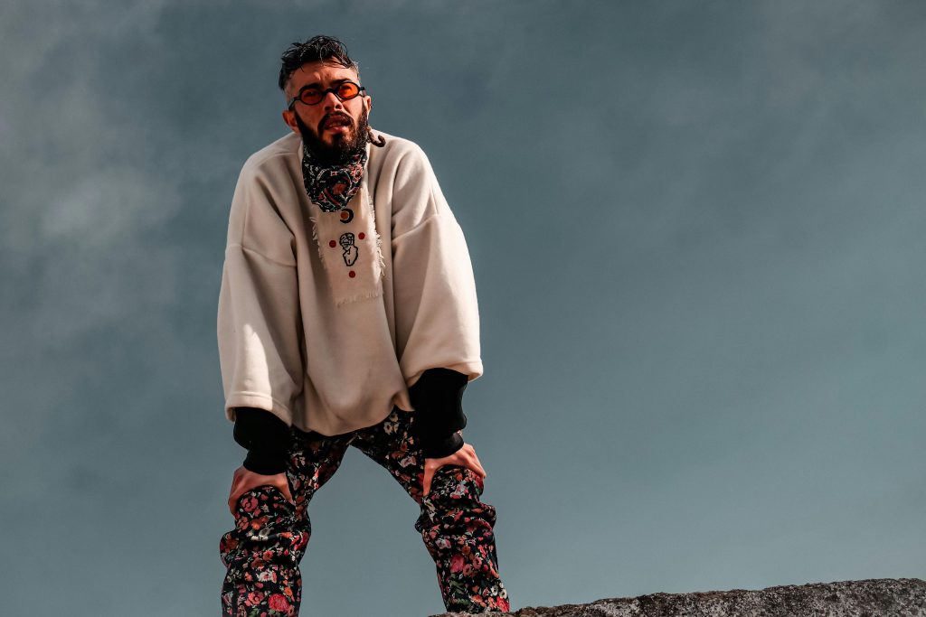 Stylish man with beard and sunglasses wearing floral pants poses confidently in a trendy fashion shoot.