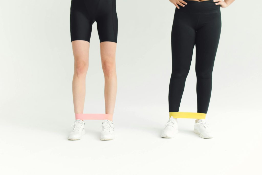 Two women in activewear using resistance bands during an indoor workout session.