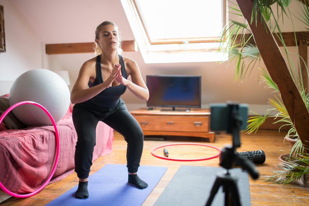 Woman performing squats at home, recording workout session on yoga mat.