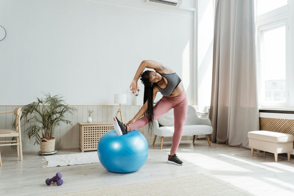 African American woman engages in fitness routine with exercise ball indoors.